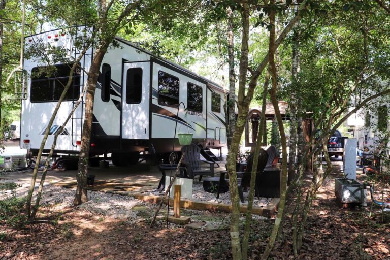 rv parked with seating outside surrounded by trees